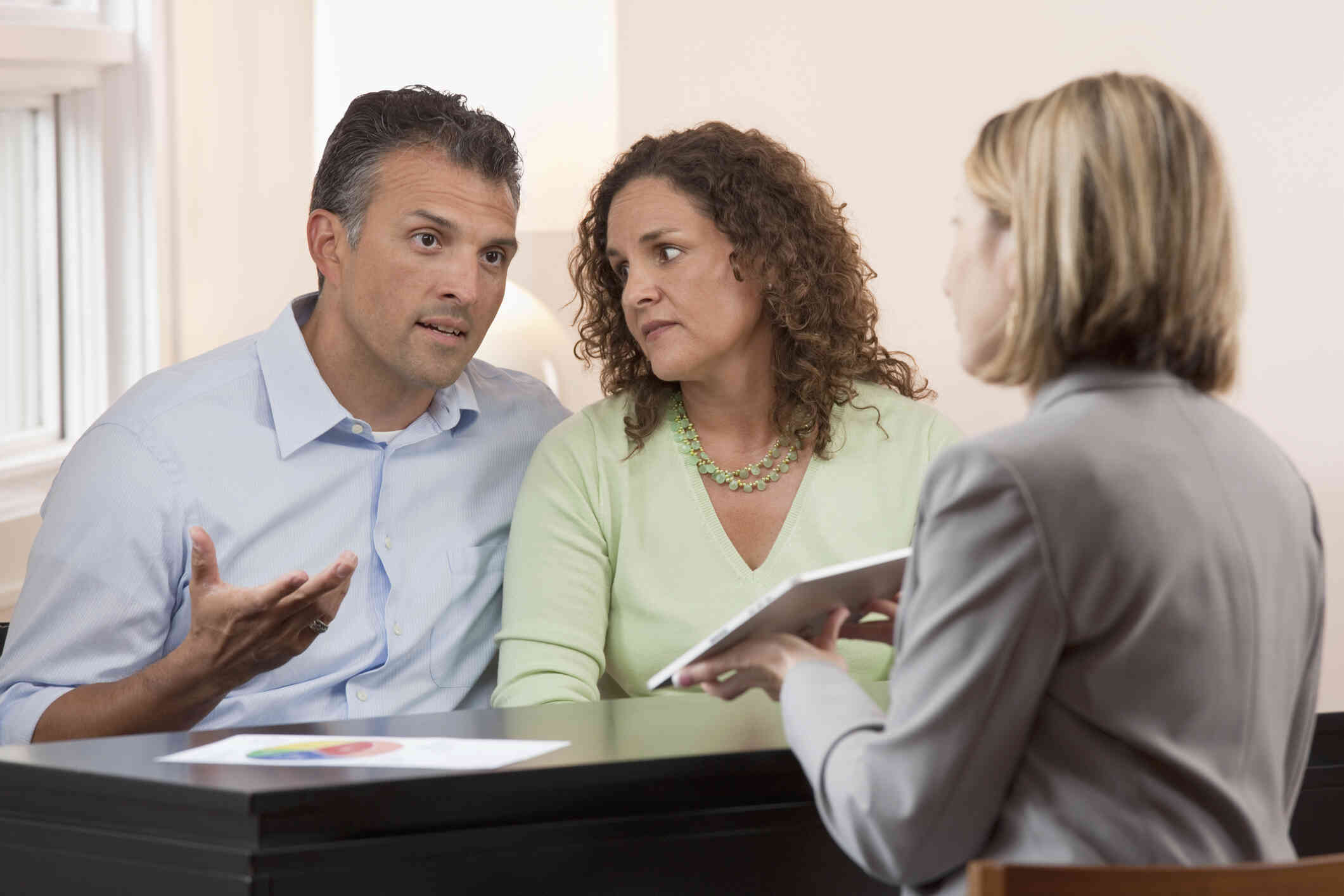 A couple engage in a serious conversation with the person holding a tablet, seated across from them.